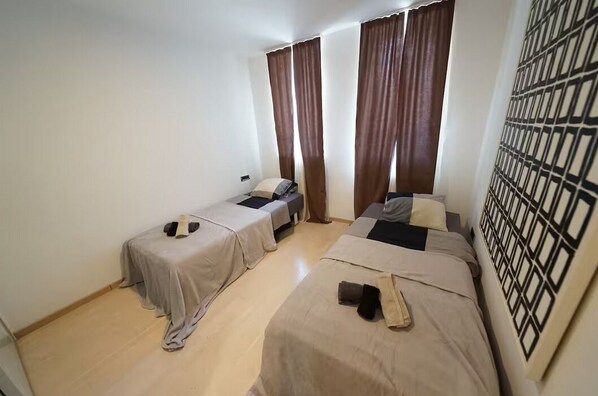 Ein Zimmer mit zwei Betten, einem fensterbelaubten Fenster und einer Wand mit Muster.