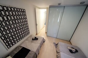 Ein kleiner, moderner Raum mit zwei Betten, einem Kleiderschrank und einer Zierleiste an der Wand.