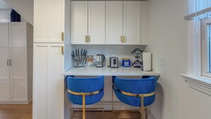 A kitchen with white cabinets, a countertop with kitchen appliances, and two blue bar stools.