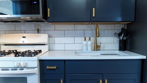 A kitchen with a white stove, a microwave, a sink with gold handles, and a cabinet with gold handles.