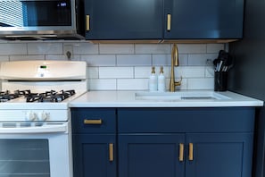 A kitchen with a white stove, a microwave, a sink with gold handles, and a cabinet with gold handles.