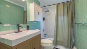 A bathroom with a shower, toilet, sink, and mirror.