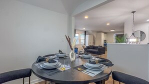 A dining area with a round table set for four, a vase with decorative elements, and a modern kitchen in the background.