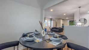 A dining area with a round table set for four, a vase with decorative elements, and a modern kitchen in the background.