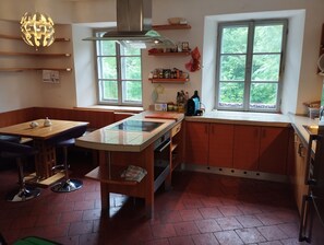 A kitchen with a central island, wooden cabinets, a window with a view, and a hanging light fixture.