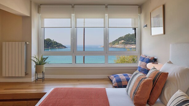A bedroom with a large window, a bed, a radiator, and a plant. - Playa de La Concha 6 by FeelFree Rentals (Donostia)