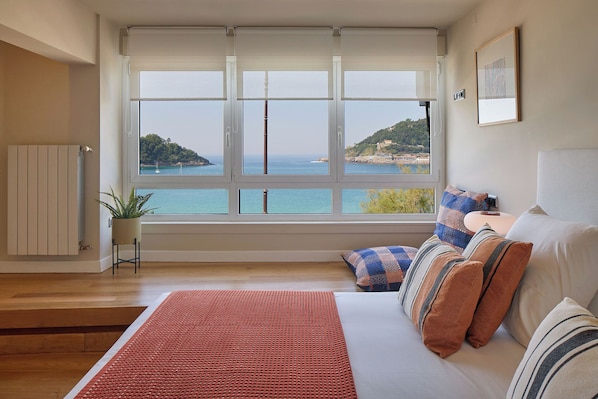 A bedroom with a large window, a bed, a radiator, and a plant. - Playa de La Concha 6 by FeelFree Rentals (Donostia)