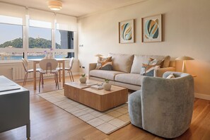 A modern living room with a sofa, armchair, coffee table, and a dining area with chairs and a table. - Playa de La Concha 6 by FeelFree Rentals (Donostia)