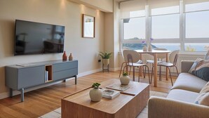 A modern living room with a flat-screen TV, grey entertainment unit, wooden coffee table, and a view of the sea through large windows. - Playa de La Concha 6 by FeelFree Rentals (Donostia)