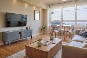 A modern living room with a flat-screen TV, grey entertainment unit, wooden coffee table, and a view of the sea through large windows. - Playa de La Concha 6 by FeelFree Rentals (Donostia)