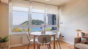 A dining area with a table and chairs, a potted plant, and a view of a coastal landscape through large windows. - Playa de La Concha 6 by FeelFree Rentals (Donostia)