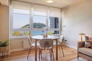 A dining area with a table and chairs, a potted plant, and a view of a coastal landscape through large windows. - Playa de La Concha 6 by FeelFree Rentals (Donostia)
