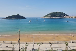 A beach with clear water, a sandy shore, and a small hill with buildings. - Playa de La Concha 6 by FeelFree Rentals (Donostia)
