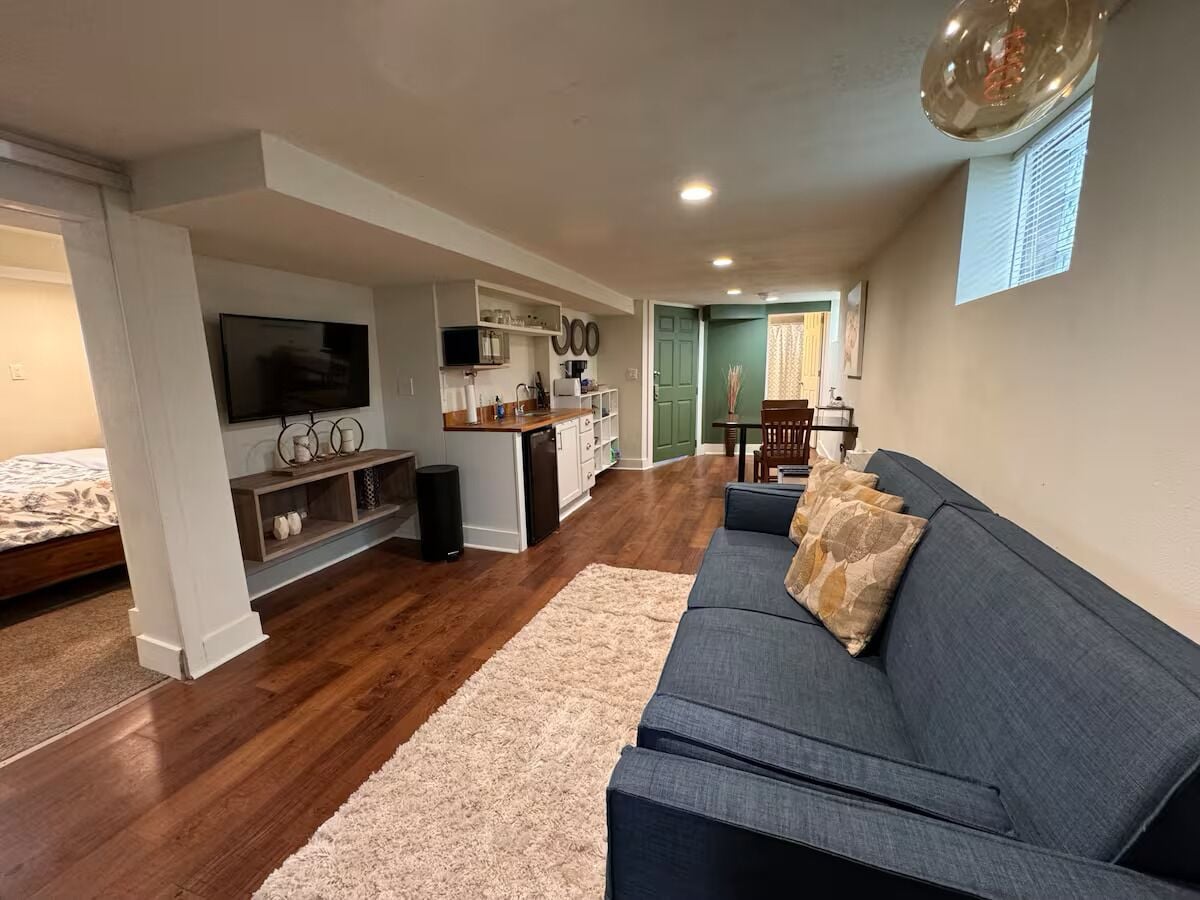 Una sala de estar moderna con un sofá oscuro, un televisor, una cocina y una mesa de comedor.