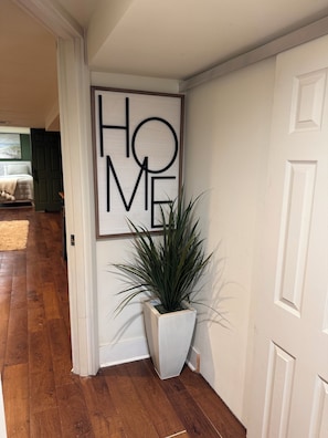 Ein Flur mit einem großen Schild mit der Aufschrift 'HOME', einer Topfpflanze und Holzboden.
