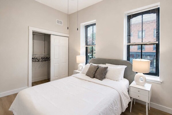 Un dormitorio con cama, lámparas de noche, armario y ventana con persianas.