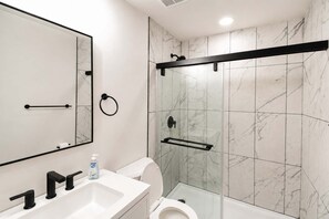 Et moderne badeværelse med hvid vask, toilet og brusekabine i glas.