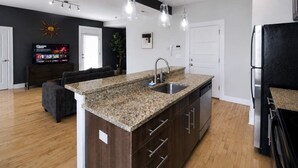A modern kitchen with granite countertops, stainless steel appliances, and a dark wood cabinet. - 1BR Opposite SLU Hospital · Parking · Long Stays (St. Louis)