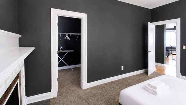 Une chambre avec un lit blanc, une cheminée blanche, un dressing et une vue sur une autre pièce.