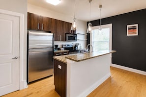 A modern kitchen with a stainless steel refrigerator, microwave, and gas stove, wooden cabinets, and a granite countertop.