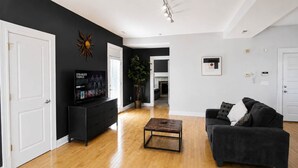 Un salon avec un canapé noir, une table basse, un téléviseur posé sur un meuble noir et une plante.
