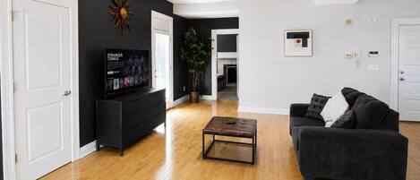 A living room with a black sofa, a coffee table, a TV on a black stand, and a plant.