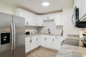 Una cocina moderna con armarios blancos, un refrigerador de acero inoxidable, horno empotrado y encimera de granito.