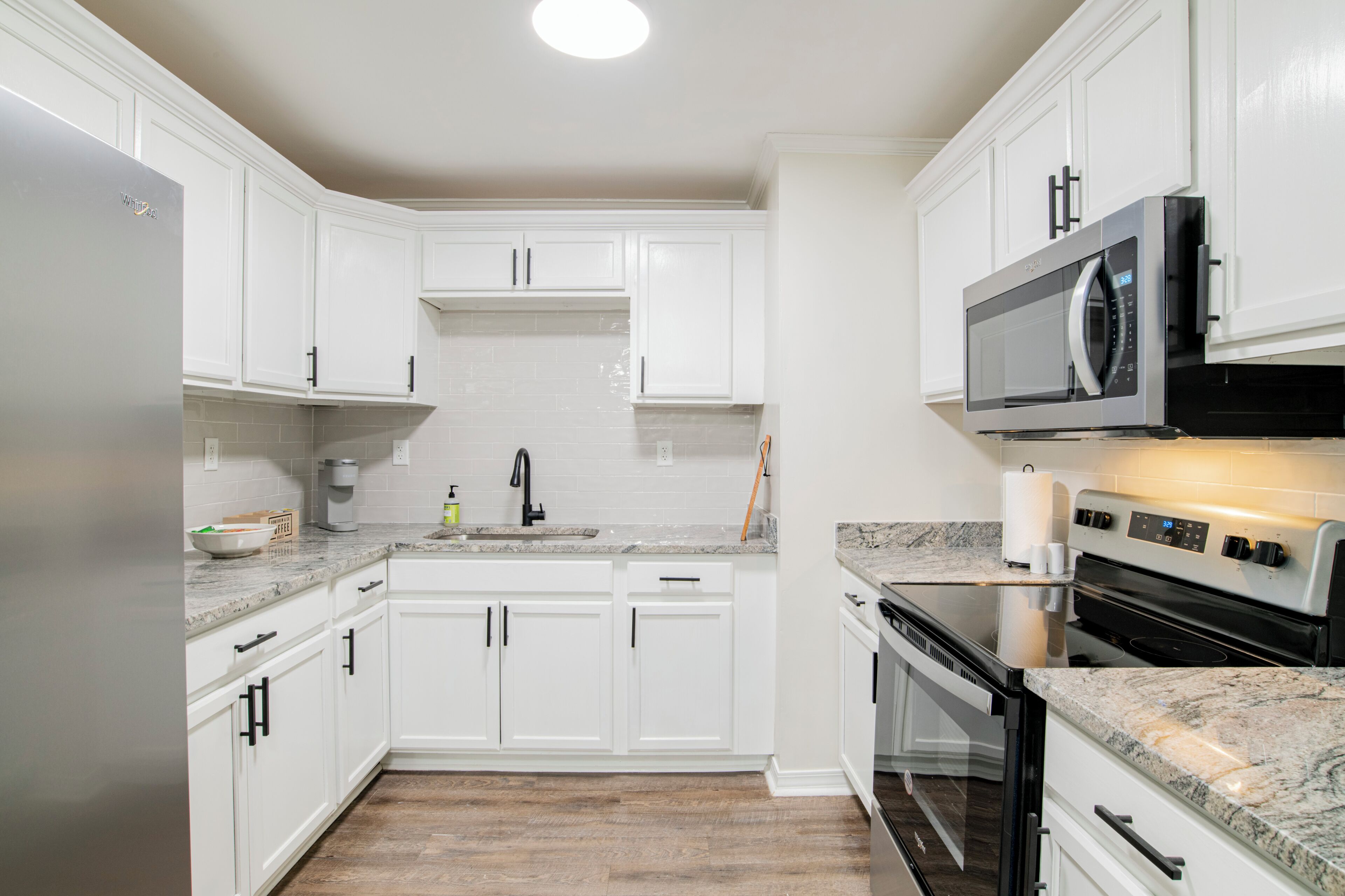 Una cocina con armarios blancos, un refrigerador de acero inoxidable, un microondas y un horno.
