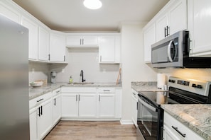 Una cocina con armarios blancos, un refrigerador de acero inoxidable, un microondas y un horno.