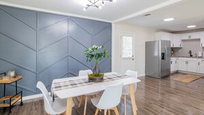 A modern kitchen with white cabinets, a stainless steel refrigerator, and a dining area with a white table and chairs.