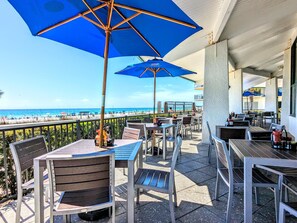 An outdoor patio with tables and chairs, blue umbrellas, and a view of the beach. - NEW to Rentals, Completely Upgraded, Desirable location 2nd floor Villa (Panama City Beach)