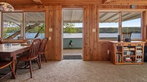 Une cabane en bois comprenant un coin repas, une bibliothèque et donnant sur un lac.