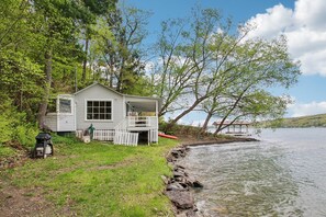 Eine Holzhütte am Seeufer mit Veranda, einer kleinen Werkstatt und einem Steg, der ins Wasser führt.