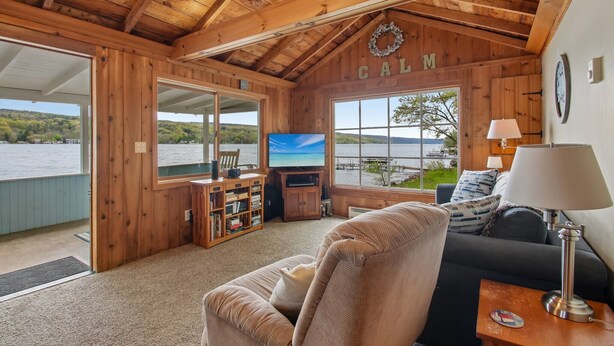 L'intérieur d'un chalet en bois, avec un téléviseur, un canapé et une vue sur un lac.