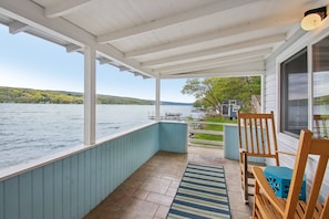 A covered outdoor area with a view of a lake, a wooden chair, and a blue table. - Chipmunk Cottage | Cozy Lakefront Escape (Penn Yan)