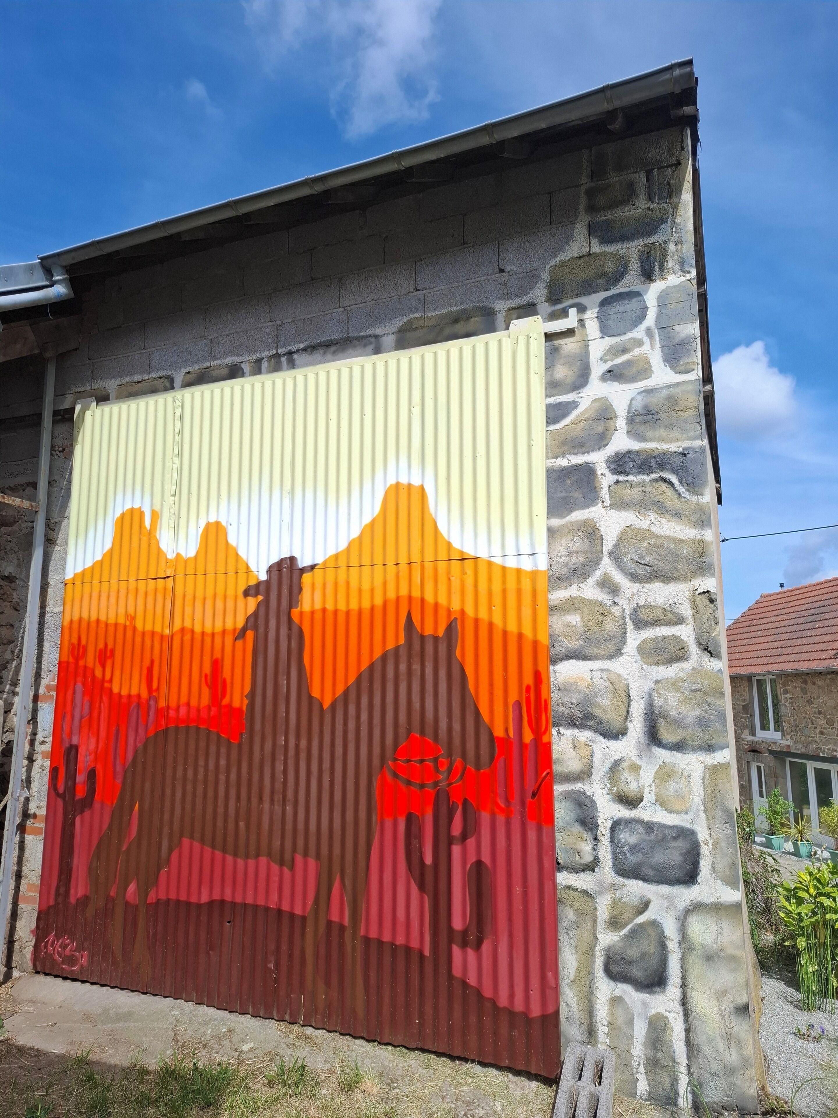 Pared de metal corrugado con un mural pintado de paisaje desértico, incluyendo un caballo y cactus.