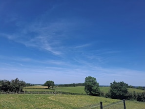 Ländliche Landschaft mit offenen Feldern, Bäumen und blauem Himmel.