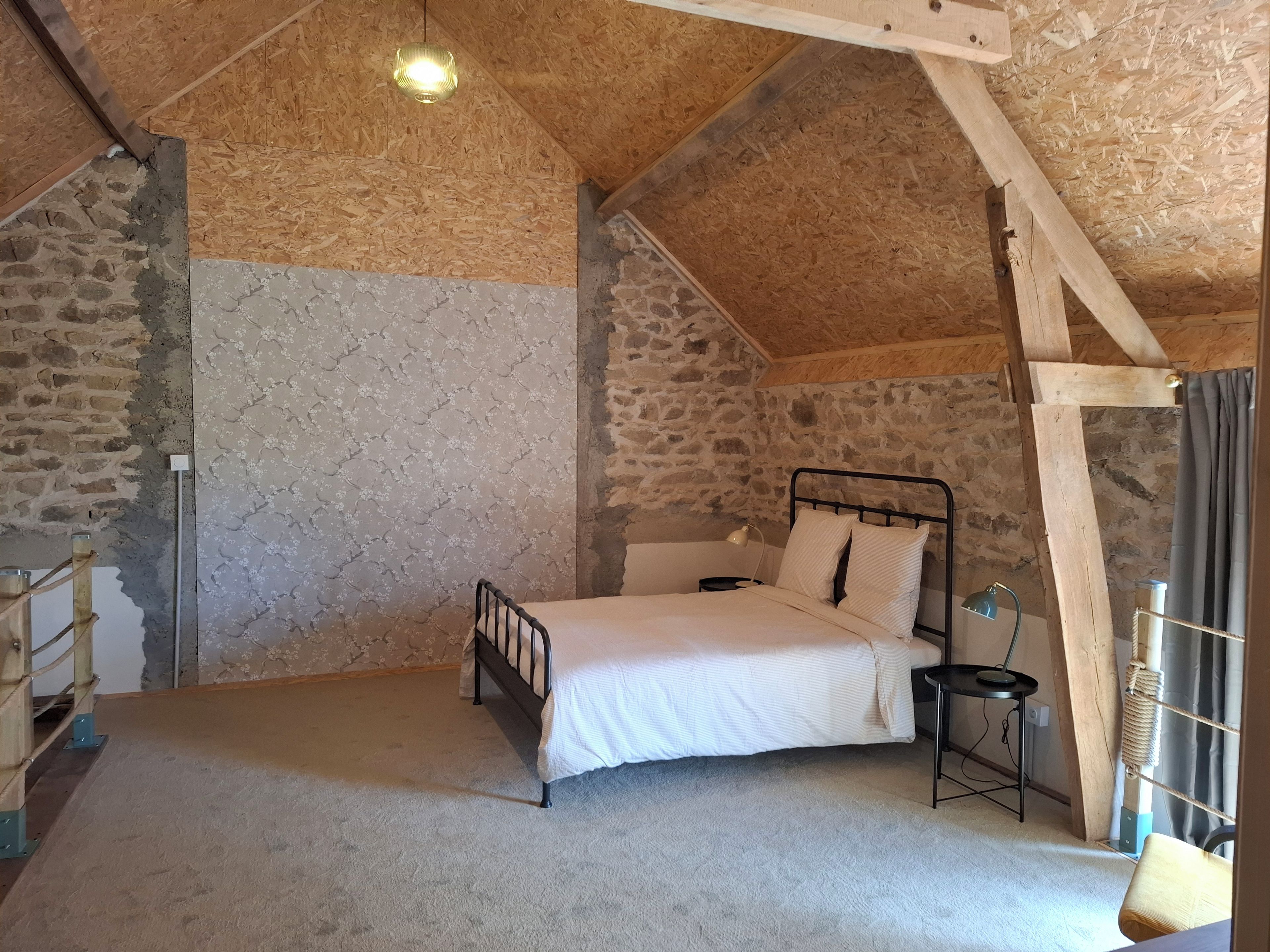 A bedroom with a sloped ceiling, a bed, a bedside table, a lamp, and a window with curtains.