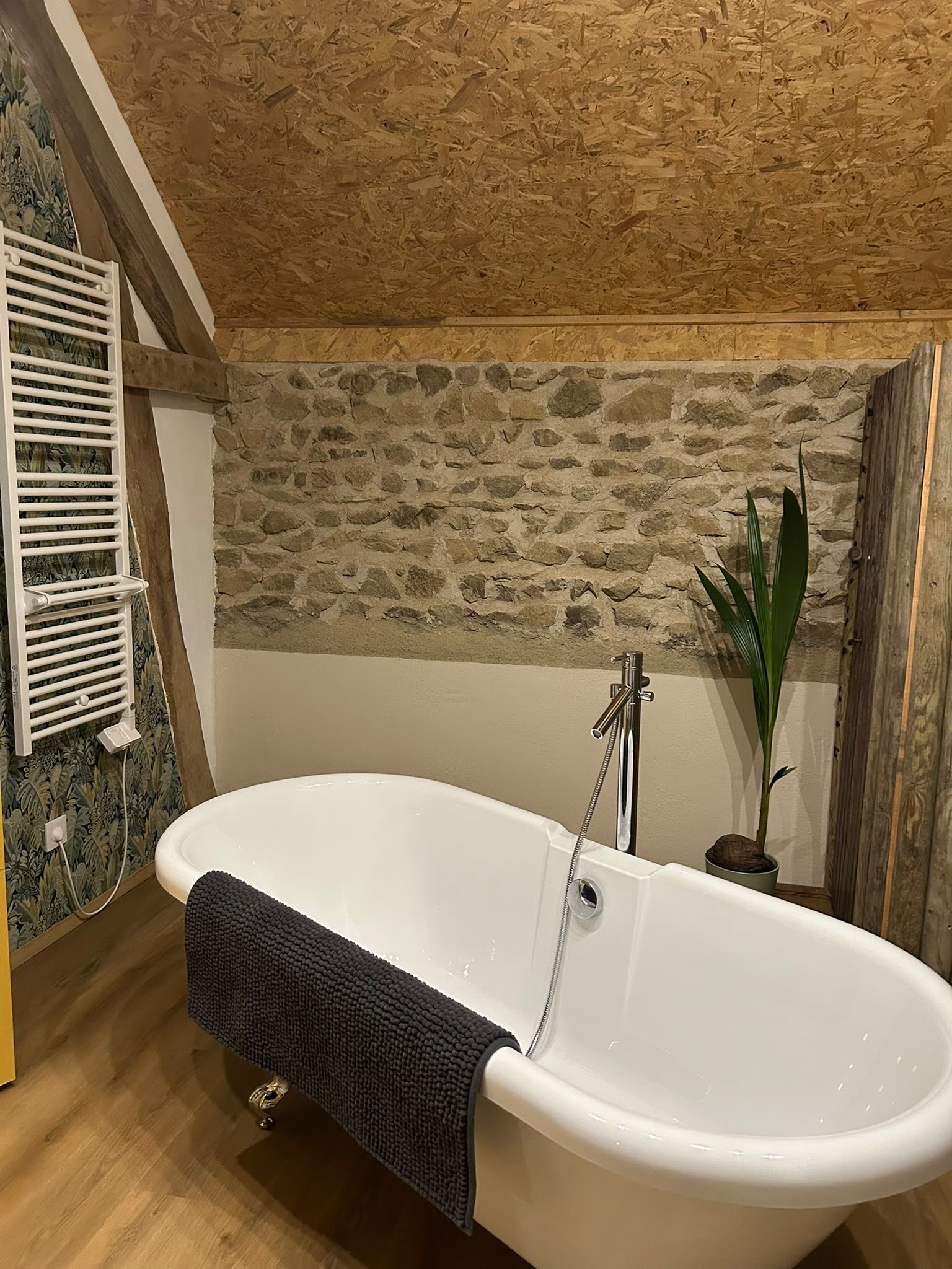 Een badkamer met een vrijstaand bad, een stenen muur en een houten plafond.