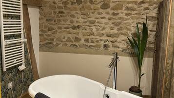 Een badkamer met een vrijstaand bad, een stenen muur en een houten plafond.