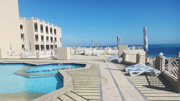A rooftop pool area with a clear view of the ocean, a building with balconies, and lounge chairs. - Sasha Collection at Stone Heights -AC, Pool & Secure (Hurghada)