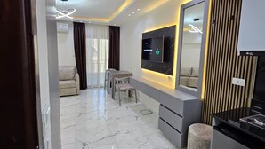 A modern living room with a TV, sofa, and dining area. - Sasha Collection at Stone Heights -AC, Pool & Secure (Hurghada)