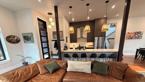 Ein modernes Wohnzimmer mit einem braunen, ledernen Ecksofa, einem gemusterten Teppich und einer Küche im Hintergrund.
