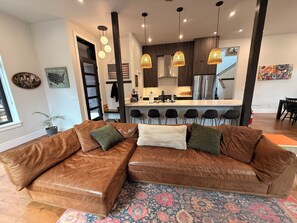 A modern living room with a brown leather sectional sofa, a patterned rug, and a kitchen in the background.