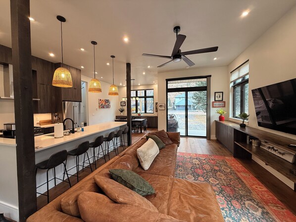 A modern kitchen with a bar area, a large sofa, and a television.