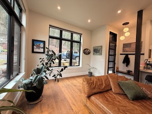 A living room with a brown leather sofa, a large window with a view of a vehicle outside, and a potted plant on the windowsill.