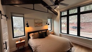 Ein Schlafzimmer mit einem Bett, zwei Nachttischen, einem Deckenventilator und großen Fenstern.