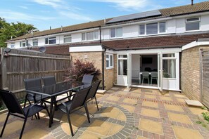 A residential property with a patio area, a glass door leading to a room, and a brick wall. - 4BR Spacious Home | Garden & Parking | Long Term (Hertfordshire)