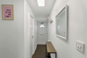 A hallway with a white door, a bench, a mirror, and a sign on the wall. - 4BR Spacious Home | Garden & Parking | Long Term (Hertfordshire)