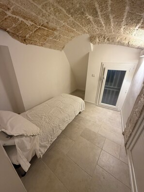 A small, single-bed room with a sloped ceiling and a door leading to a balcony. - Mediterranean Deluxe Stone House (Molfetta)